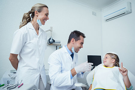 Male dentist and assistant talking to girl in the dentists chair